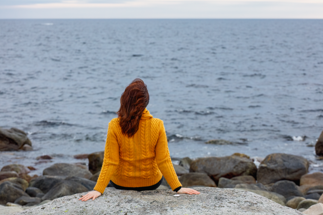 Woman sitting on rocks looking out at ocean.